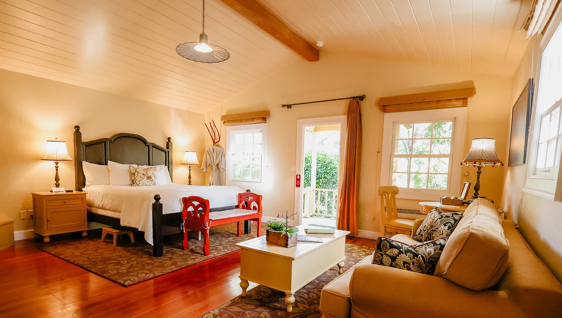 A cozy bedroom featuring a large bed, seating area, and natural light from multiple windows.